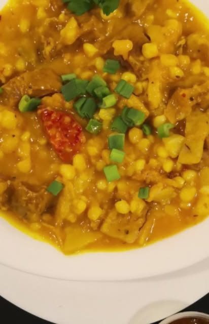 Primer plano de un locro con choclo, verdeo y ají